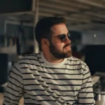 Homem de óculos escuros e camisa listrada com cabelo modelado pela Lord Shiva.