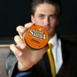 Modelo masculino segurando a pomada Power Brilho em primeiro plano, vestindo terno e gravata.